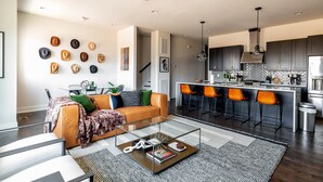 Ein modernes Wohnzimmer mit einem Glastisch, einer Couch mit Kissen und einem Essbereich mit Barhocker.