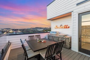 A rooftop patio with a wooden table, chairs, and a grill.