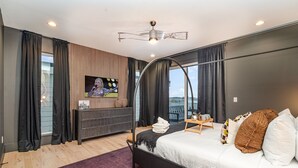 Ein modernes Schlafzimmer mit Bett, Fernseher, Balkon und Blick auf die Stadt.
