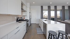 Een moderne keuken met witte kastjes, een roestvrijstalen fornuis en een groot kookeiland met barkrukken.