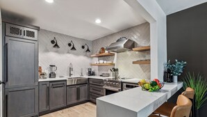 Une cuisine moderne avec des meubles gris, un îlot central en marbre blanc et un dosseret orné d’un motif en chevrons.