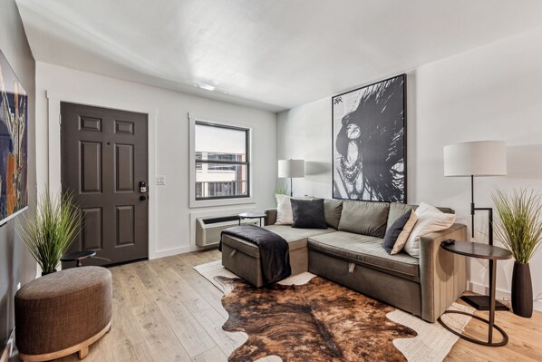 A modern living room with a sectional sofa, a large abstract painting, a floor lamp, and a cowhide rug. - Lyric Loft - Music Row - 4 Mins to Broadway (Nashville)