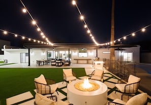 Un patio al aire libre con una fogata, asientos e iluminación colgante.
