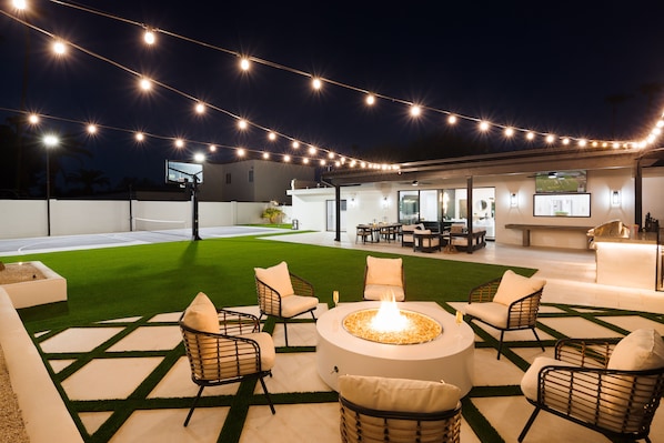 Un área de patio al aire libre con un hogar para fuego, asientos e iluminación colgante.