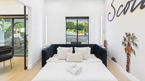 Een moderne hotelkamer met een groot bed en uitzicht op de omgeving, met een muur waarop de naam 'Scott' gedeeltelijk zichtbaar is.