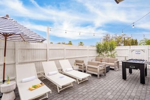 Une terrasse extérieure avec des fauteuils confortables, une table de baby-foot et des guirlandes lumineuses.