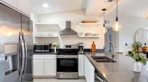 Une cuisine moderne dotée d’appareils électroménagers en acier inoxydable, de meubles blancs et d’un éclairage suspendu.
