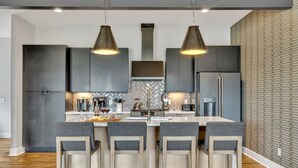 Een moderne keuken met donkere kasten, een centraal eiland met barkrukken en hanglampen.