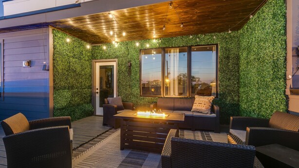 Een terras buiten met een houten tafel en stoelen, omringd door groen en lichtslingers.