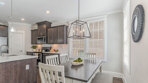 A modern kitchen with dark cabinets, a central island, and a dining area with a wooden table and chairs. - Ivory - Private Porch - Walk to Centennial Park (Nashville)
