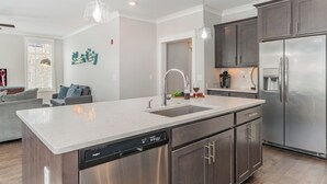A modern kitchen with stainless steel appliances, a dishwasher, and a large island. - Ivory - Private Porch - Walk to Centennial Park (Nashville)