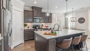 A modern kitchen with dark wood cabinets, stainless steel appliances, and a large island with bar stools. - Ivory - Private Porch - Walk to Centennial Park (Nashville)