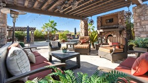 An outdoor patio area with wicker furniture, stone pillars, and a stone fireplace. - Estrella-resort Style Pool&yard-estrella Mountain (Goodyear)