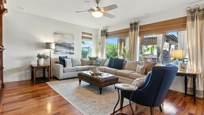 A spacious living room with a wooden floor, a ceiling fan, a beige sofa set, a blue armchair, and a coffee table. - Estrella-resort Style Pool&yard-estrella Mountain (Goodyear)