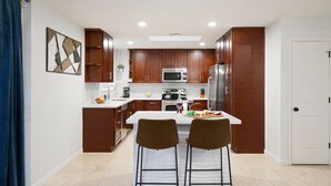 Una cocina moderna con armarios de madera, una isla central con dos sillas y una mesa de comedor lista para comer y beber.