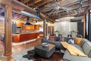 Una cocina moderna con una isla central, un comedor con sofá y mesa de centro, y una sala de estar con un ventanal grande.