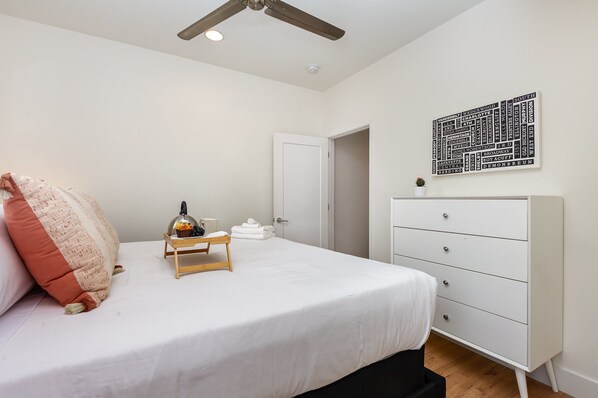 A bedroom with a bed, a white dresser, a ceiling fan, a wall art piece, and a door. - Citrine-private Patio & Balcony-near Germantown (Nashville)