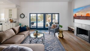 A spacious living area with a sofa, armchair, and coffee table, a fireplace, and a large window with a view of the outdoors. - Majestic Mountain Mansion-heated Pool-guest House (Paradise Valley)
