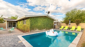 A swimming pool with a swan float, surrounded by yellow lounge chairs and a covered patio area with a satellite dish. - Sunhaven -pool Heat Available - Walk to Old Town (Scottsdale)