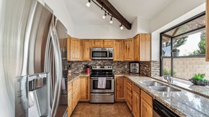 A modern kitchen with wooden cabinets, stainless steel appliances, granite countertops, and a large window providing natural light. - Sandyland-private Pool-mins 2 Waste Management TPC (Scottsdale)