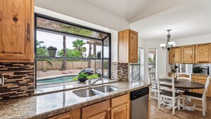 A kitchen with granite countertops, wooden cabinets, a built-in dishwasher, and a view of a pool and palm trees. - Sandyland-private Pool-mins 2 Waste Management TPC (Scottsdale)