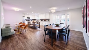 Een moderne keuken met witte kastjes, een eethoek met een houten tafel en stoelen, en een zithoek met een bank en fauteuils.