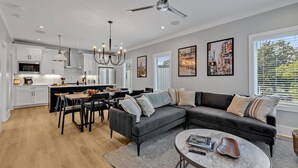 A modern kitchen with white cabinets, a dining area with a black table and chairs, a black sectional sofa, and a round coffee table. - Tenor - Private Rooftop - 8 Mins to Broadway (Nashville)