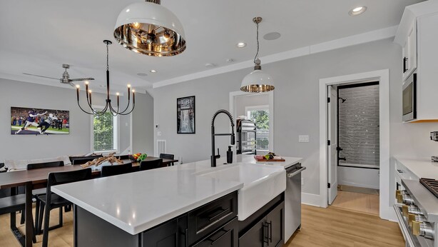 A modern kitchen with a central island, pendant lighting, and a dining area with a large TV. - Tenor - Private Rooftop - 8 Mins to Broadway (Nashville)