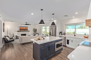 A modern kitchen with a central island, white cabinetry, and a large window providing natural light. - Greenway Getaway - Private Pool - North Scottsdale (Scottsdale)