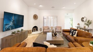 A modern living room with a large flat-screen TV, leather sofas, a coffee table, and a fireplace.