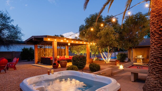 A hot tub surrounded by outdoor seating, string lights, and a barbecue area.