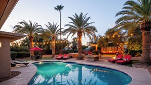 A swimming pool with lounge chairs and palm trees, surrounded by string lights.