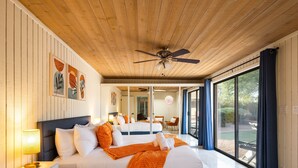 A spacious bedroom with a large bed, a ceiling fan, and a view of the outdoors through a sliding glass door.