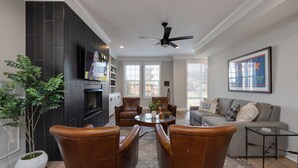 A living room with a fireplace, leather chairs, a sofa, a coffee table, and a ceiling fan. - Gulch Melody - Private Rooftop - Heart of Gulch (Nashville)