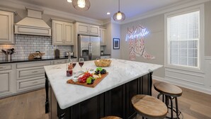 A kitchen with a marble island, white cabinets, stainless steel appliances, pendant lights, and a neon sign. - Gulch Melody - Private Rooftop - Heart of Gulch (Nashville)