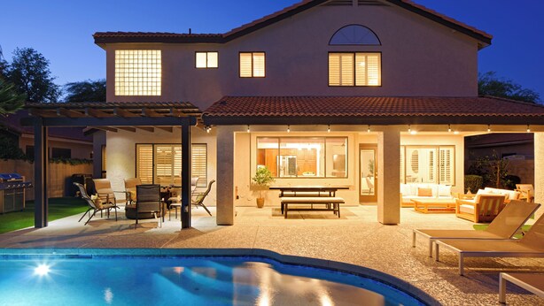 Una casa de dos pisos con piscina, mobiliario exterior y un patio cubierto.