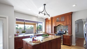 Una cocina amplia con una isla grande, armarios de madera, protector contra salpicaduras de piedra y vistas al exterior.
