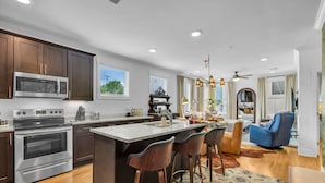 A modern kitchen with dark wood cabinets, stainless steel appliances, and a central island with bar stools. - Woodwind - Minutes to Broadway -walk to Breweries (Nashville)