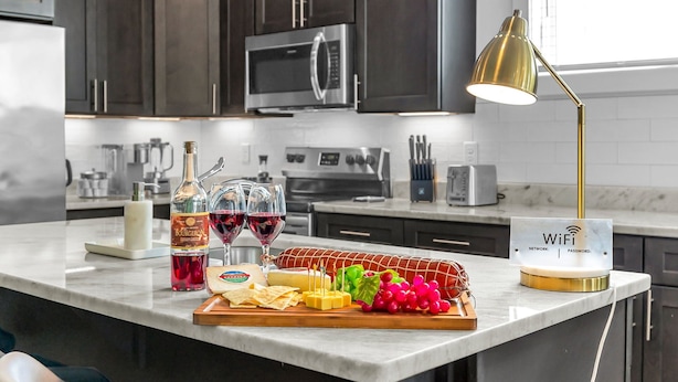 A modern kitchen with dark cabinets, stainless steel appliances, a marble countertop, and a WiFi password sign. - Woodwind - Minutes to Broadway -walk to Breweries (Nashville)