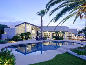 Una casa moderna con piscina, mobiliario exterior y palmeras.
