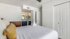 A bedroom with a bed, a ceiling fan, a white door, and a bathroom visible through an open door. - Blue Abode - Old Town Scottsdale - Pool &bbq Grill (Scottsdale)