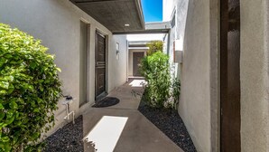 A narrow, covered outdoor corridor with a concrete ceiling, a door with a metal gate, and a small garden area with gravel and plants. - Blue Abode - Old Town Scottsdale - Pool &bbq Grill (Scottsdale)