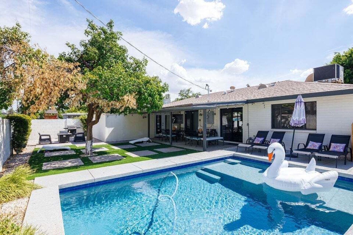 Un patio trasero con piscina, un flotador con forma de cisne y un porche cubierto.