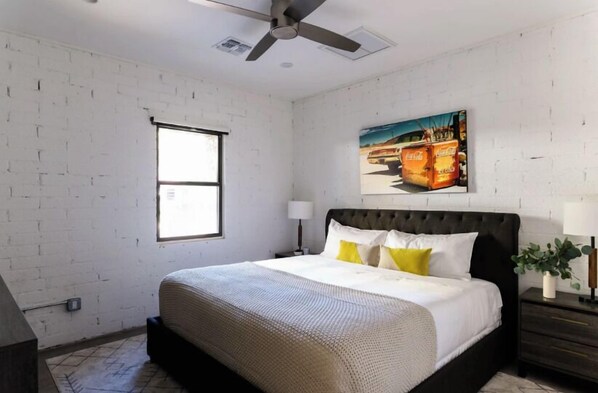 A bedroom with a large bed, a ceiling fan, a window, and a painting on the wall.