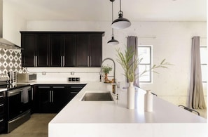 A modern kitchen with dark cabinets, a white countertop, a large sink, and pendant lighting. - Nova-in the Middle of Old Town-walk to Everything! (Scottsdale)