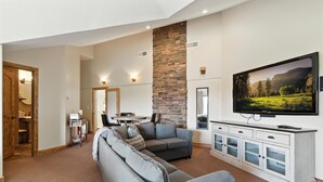 Un salon avec un canapé d’angle, un téléviseur à écran plat fixé au mur, un mur d’accent en pierre et un coin repas à l’arrière-plan.