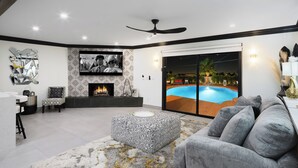 A modern living room with a fireplace, a television, and a pool visible through glass doors. - Modern Roose-pool Heat Available-hot Tub- Old Town (Scottsdale)