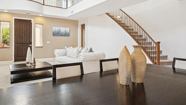 Un vaste espace de vie agrémenté d’une table basse en bois foncé, d’un canapé blanc et de deux vases à motifs. Un escalier en bois, doté d’une rampe, mène à l’étage supérieur.