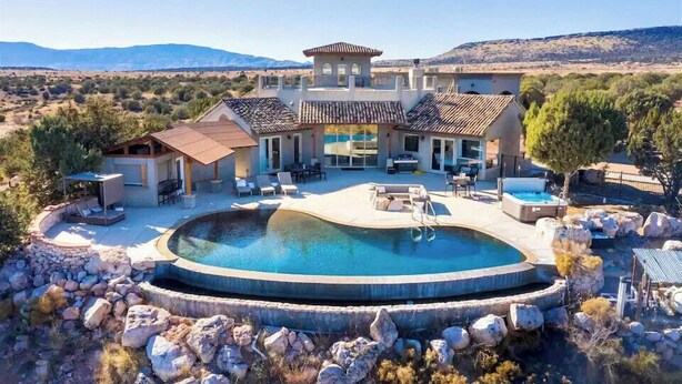 A large house with a swimming pool, outdoor seating, and a view of the mountains.