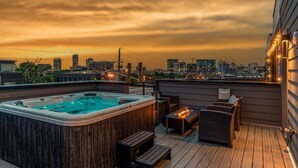 Terraço no telhado com hidromassagem, móveis de vime e vista para o horizonte da cidade ao pôr do sol.